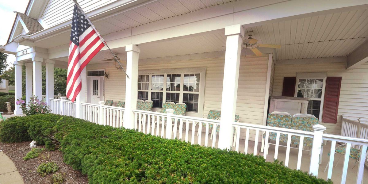 A charming porch with white columns and an American flag, featuring comfortable seating.