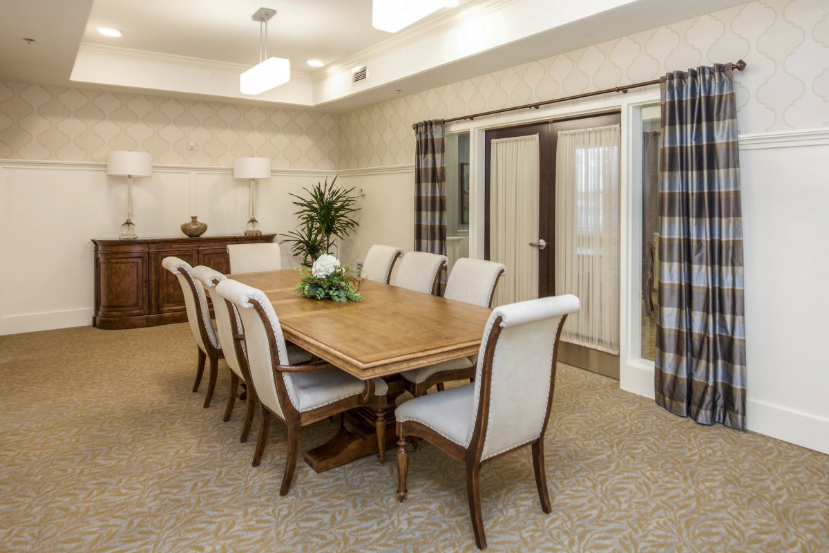 A well-decorated dining room with a large wooden table and upholstered chairs, featuring tasteful decor and potted plants.