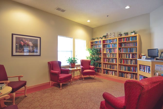 A cozy library with red chairs and a large bookshelf.