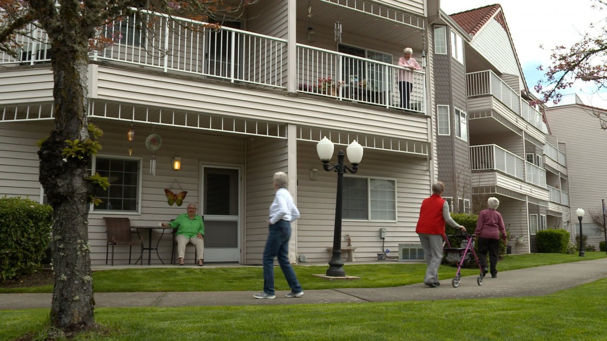 Elderly individuals walking and interacting outside an apartment building.