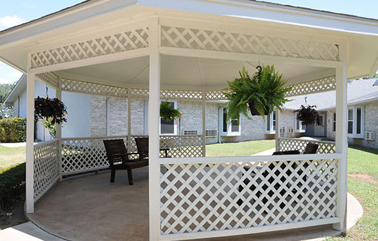 A spacious gazebo with lattice walls, hanging plants, and outdoor seating.