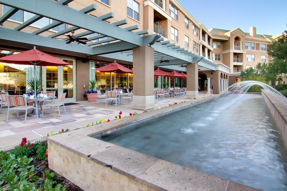 A hotel exterior with a fountain and outdoor seating area featuring red umbrellas.