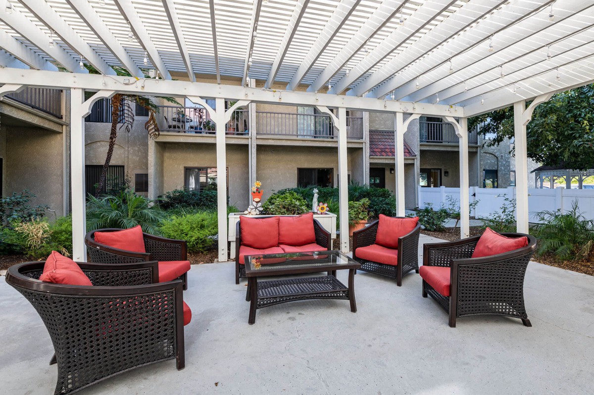 An inviting outdoor patio featuring wicker furniture with red cushions under a pergola.