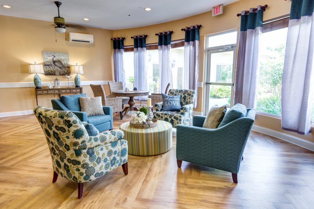 A cozy living room with multiple chairs, a small table, and large windows with curtains.