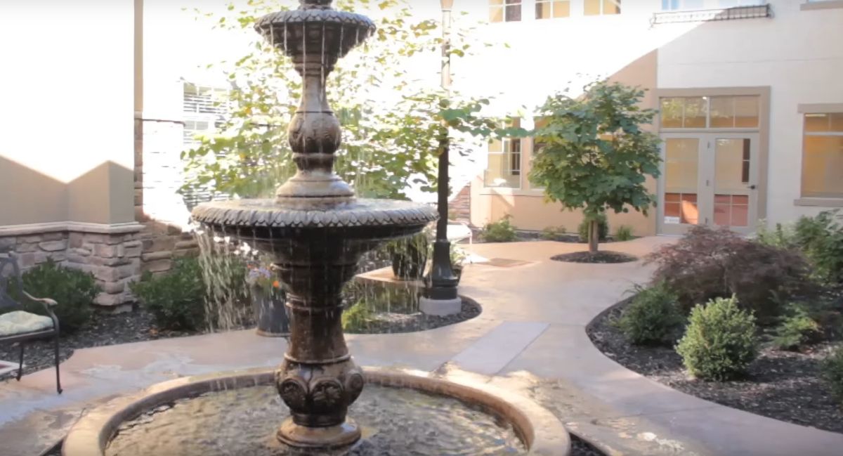 A tranquil courtyard featuring a two-tiered fountain surrounded by landscaped pathways and greenery.