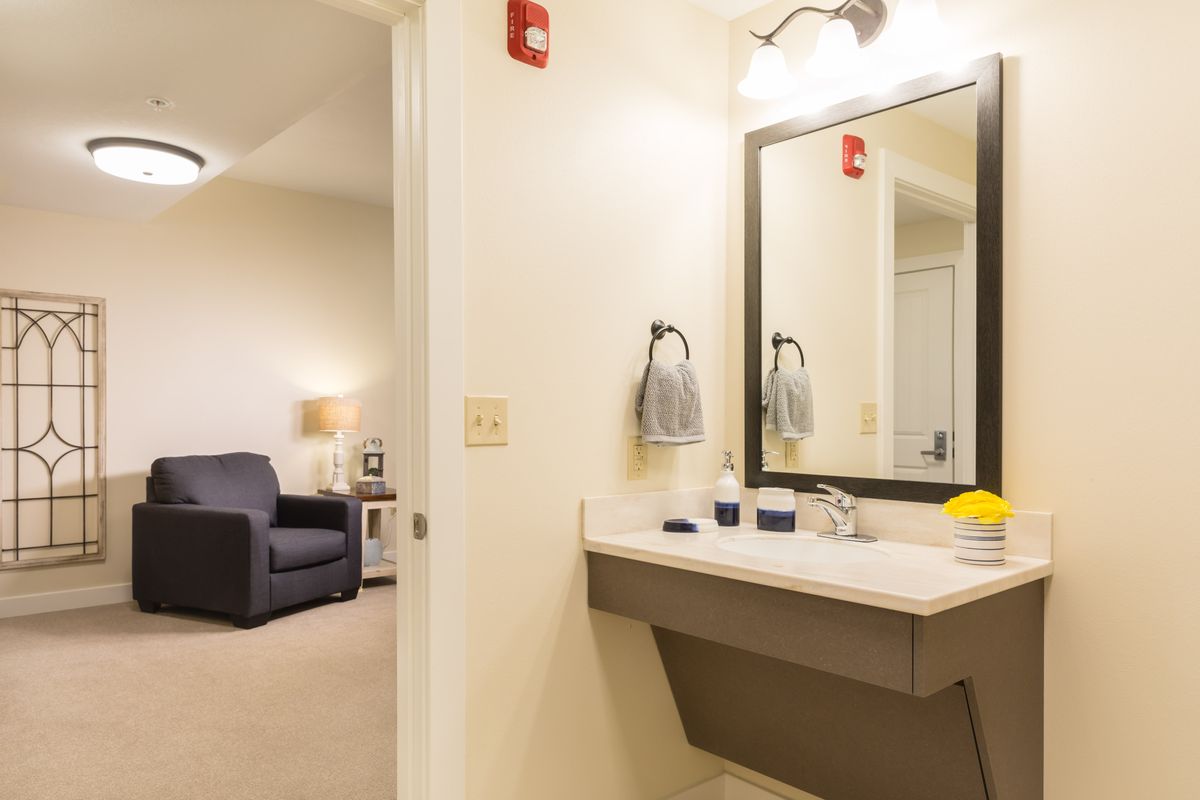 A view of a bathroom with a sink and mirror, adjacent to a living area with furniture.