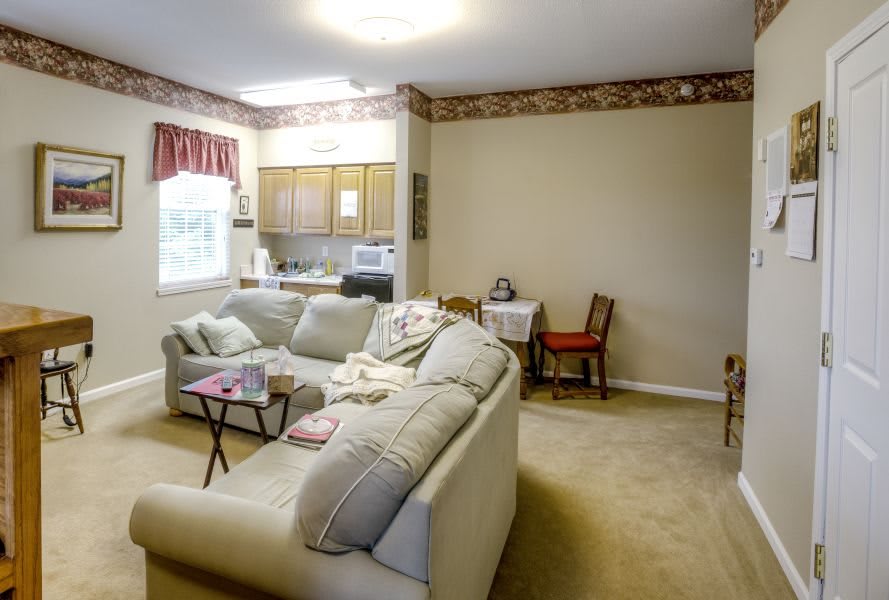 A cozy living room features a comfortable sofa, small dining area, and a view into the kitchen.