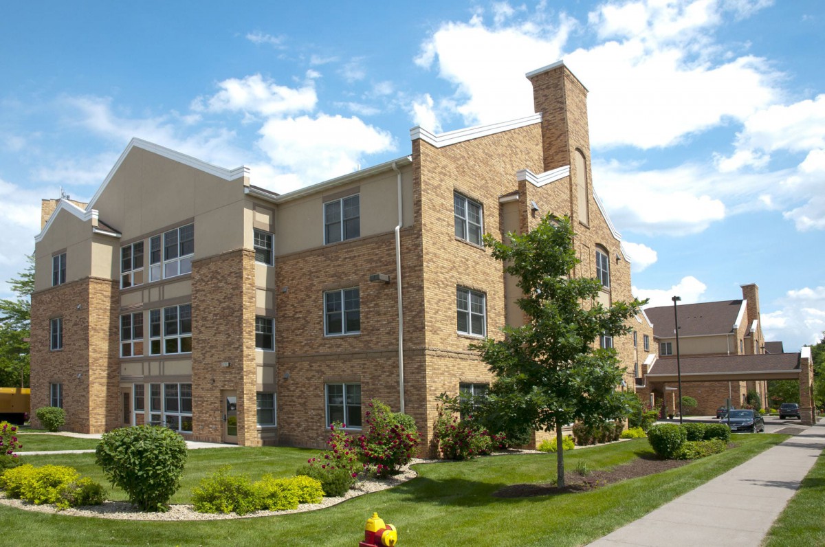 A brick residential building with a well-maintained lawn and trees under a partly cloudy sky.