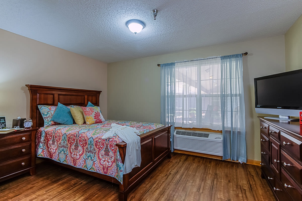 A cozy bedroom with a wooden bed, colorful bedding, and a large window with sheer curtains.