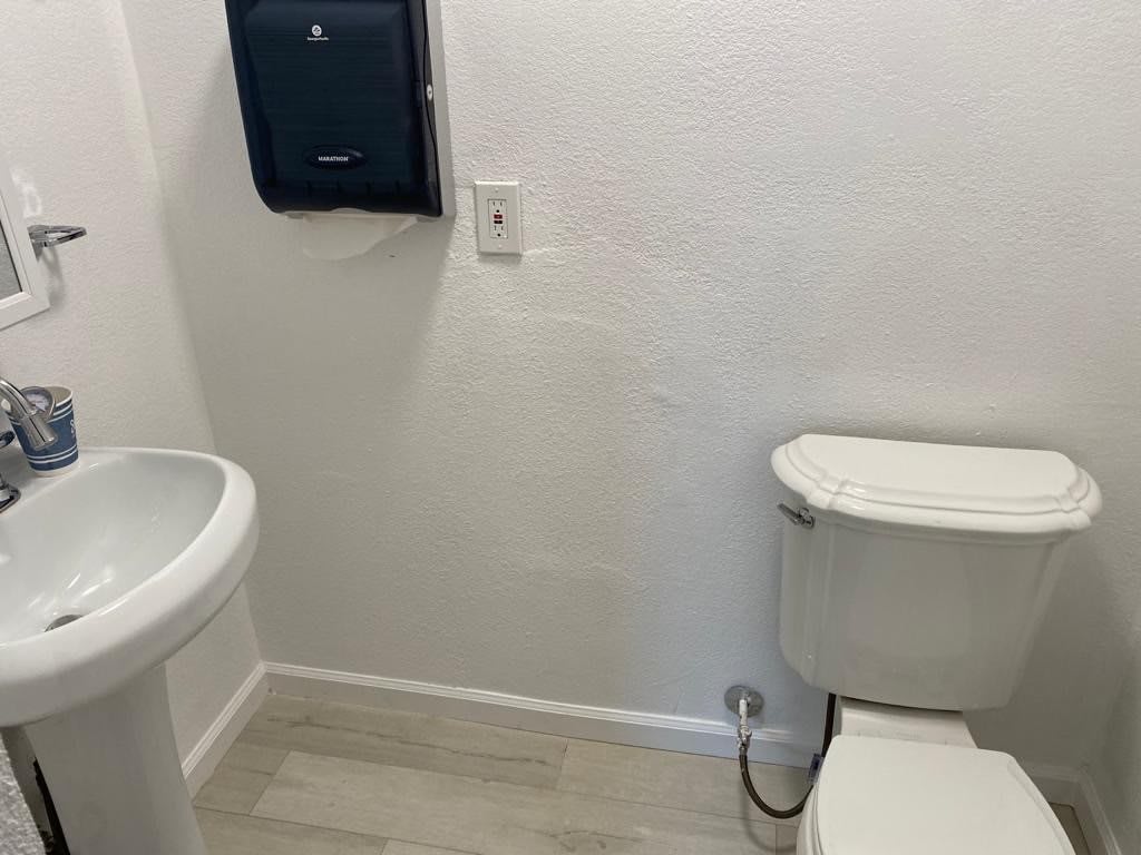 A simple bathroom with a toilet, sink, and paper towel dispenser.