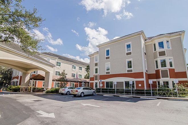 A view of a hotel building with a parking lot and cars under a cloudy sky.