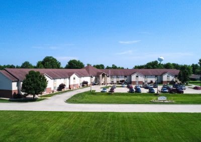 A suburban residential complex with a parking lot and a spacious lawn under a clear blue sky.