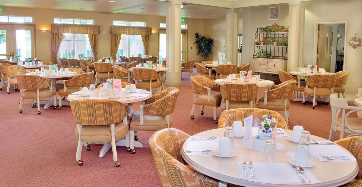 A spacious restaurant dining area with empty tables and chairs, featuring warm decor and natural light.