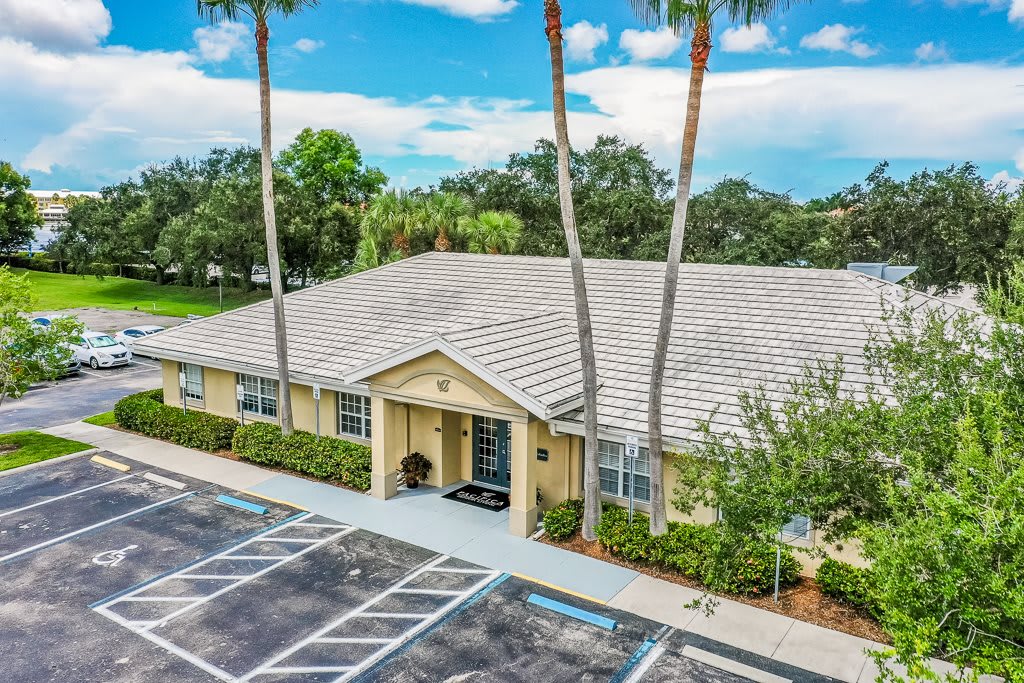 A single-story building with a parking lot and palm trees.