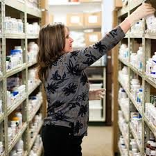 A woman organizing medication bottles on shelves in a pharmacy.