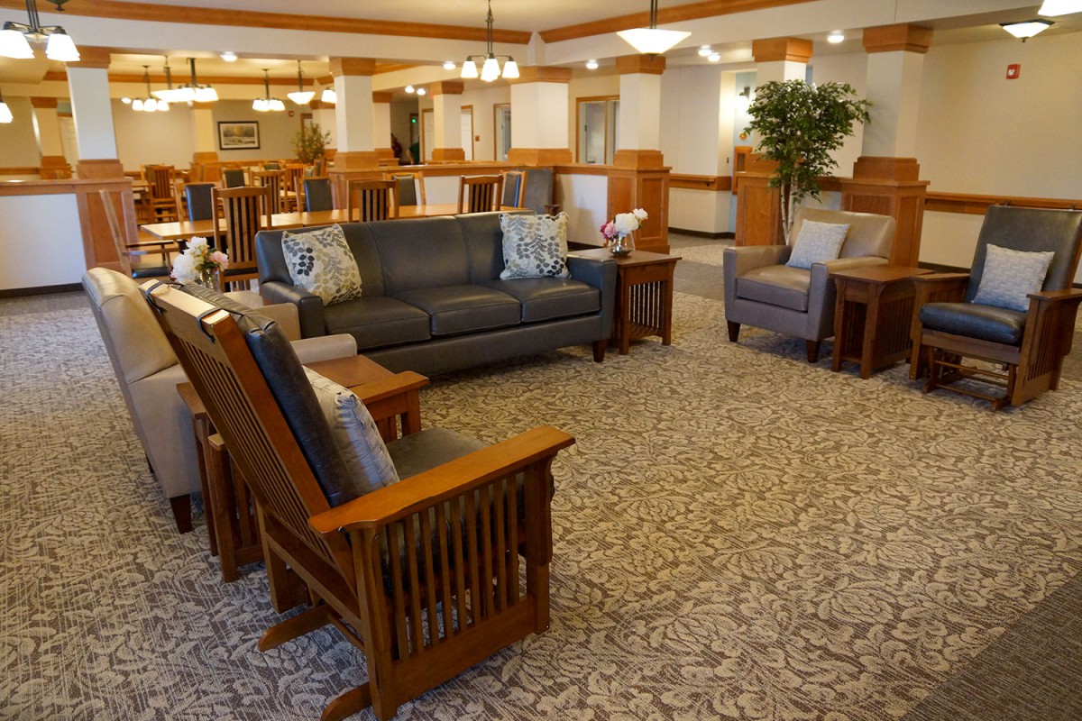A cozy living room with sofas, chairs, and a carpeted floor, featuring warm lighting and decorative elements.