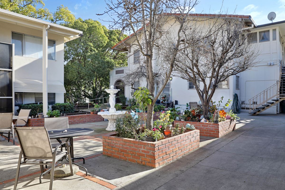 A peaceful residential courtyard featuring a central fountain, surrounded by brick planters with flowers and outdoor seating.