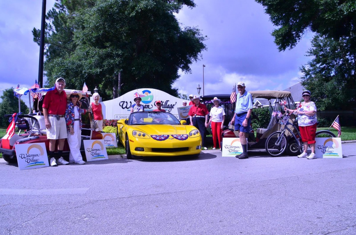 A group of people gathered around a yellow car at an outdoor event, possibly a car show.