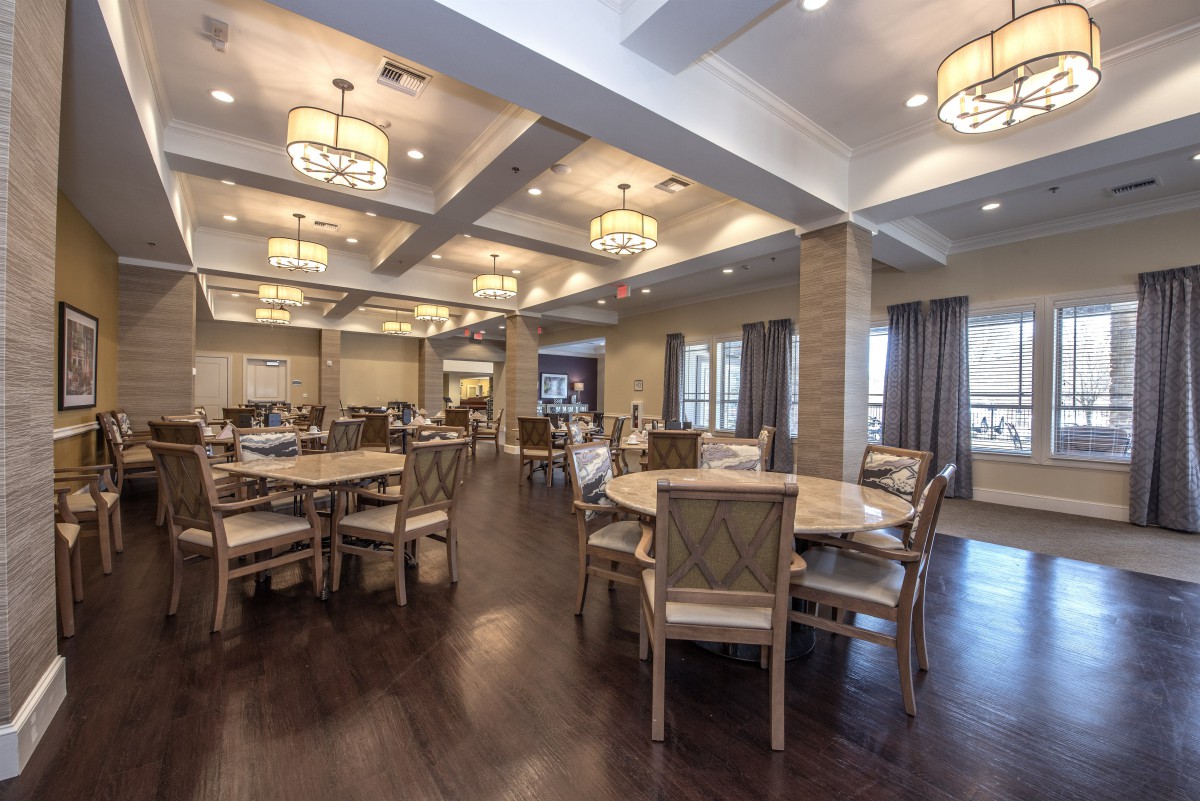 A spacious dining area with multiple round tables, chairs, and elegant ceiling lights.