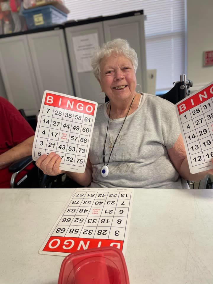 An elderly woman smiling while holding bingo cards.