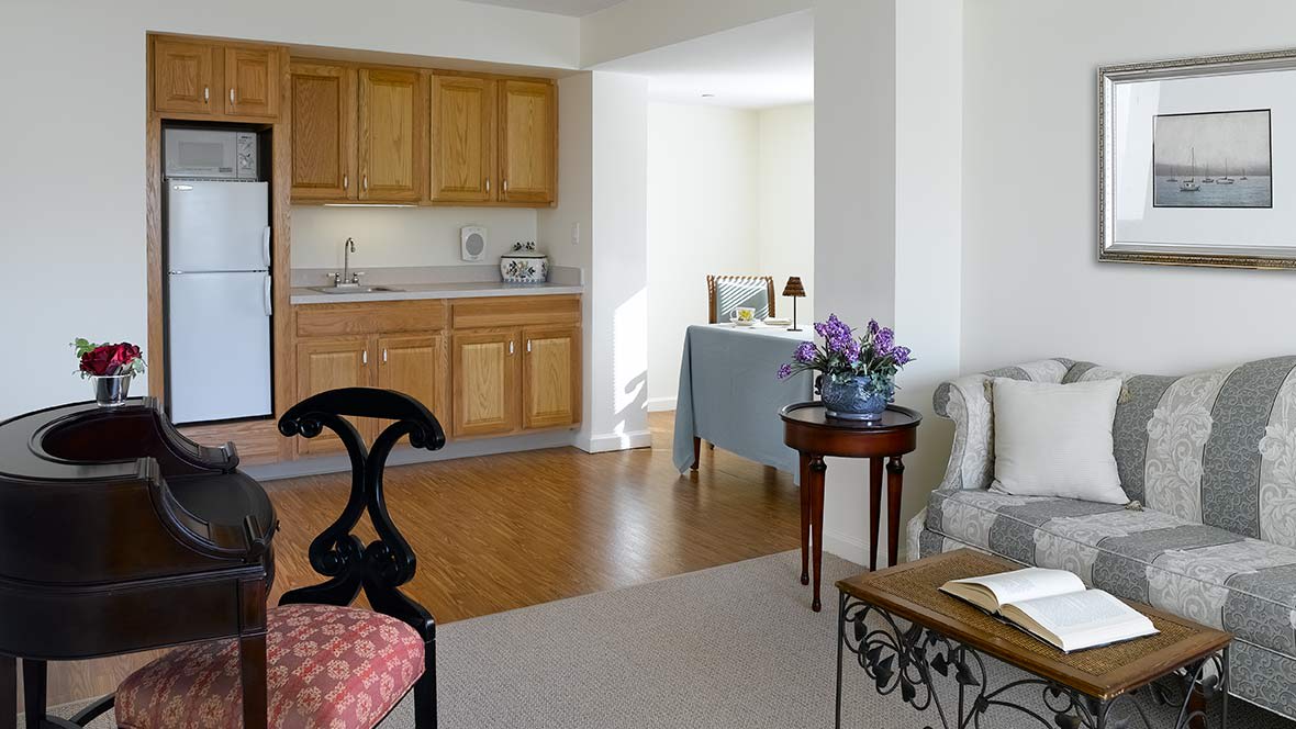 A cozy interior featuring a kitchenette with wooden cabinets, a small dining area, and a living space with elegant furniture and floral decor.