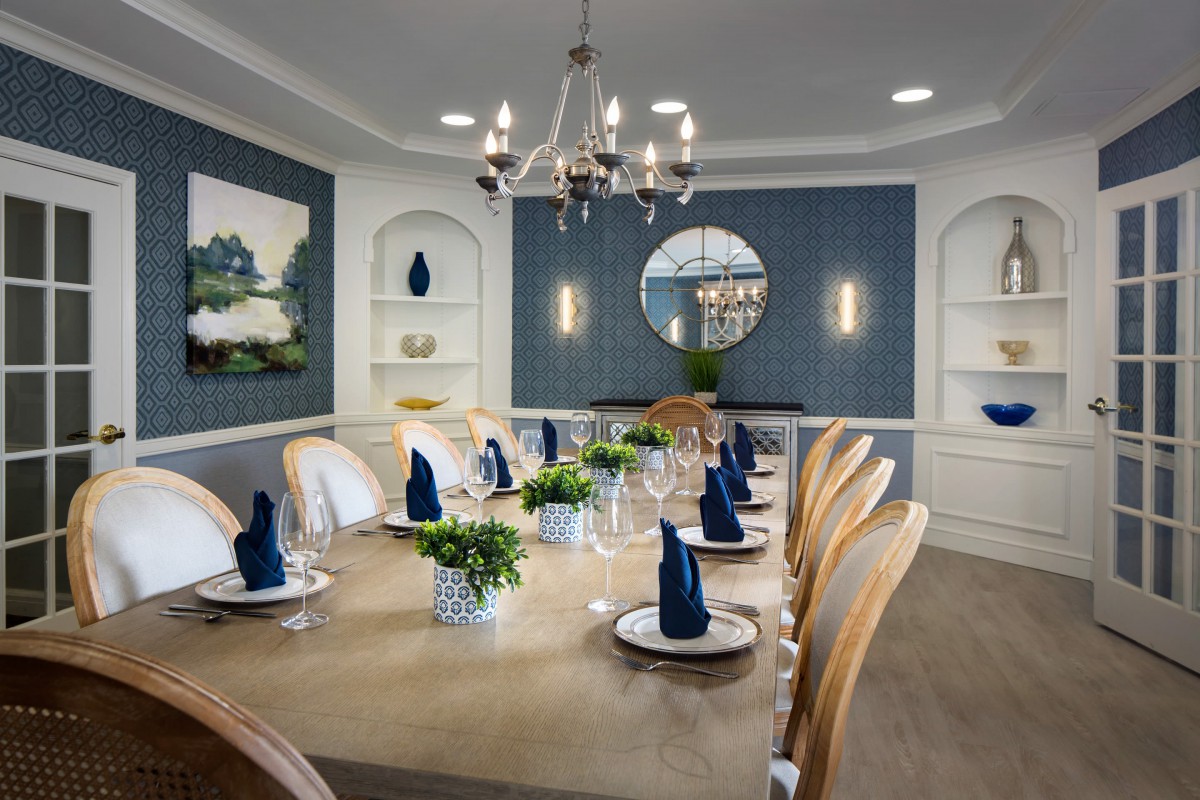 An elegantly set dining room featuring a large table with blue napkins, a chandelier, and stylish wall decor.