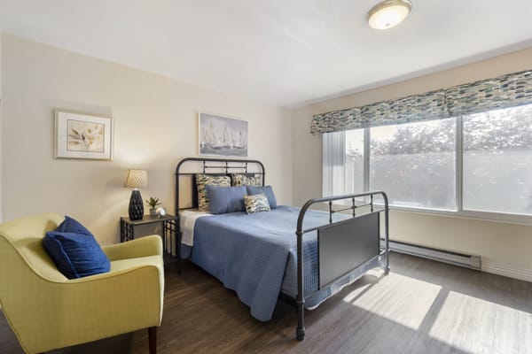A cozy bedroom with a metal bed frame and blue bedding, illuminated by natural light from a large window.