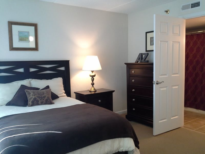 A cozy bedroom featuring a neatly made bed, a bedside lamp, and a dresser.