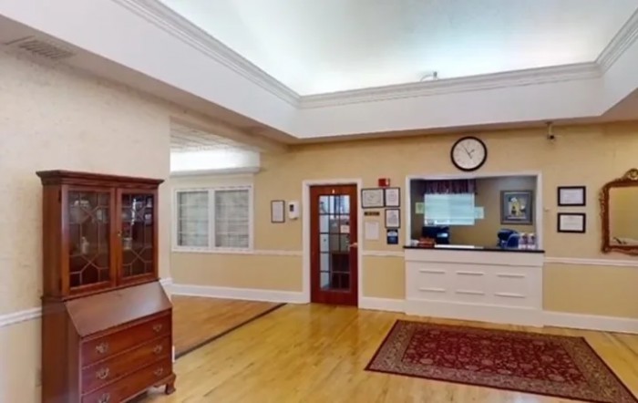 A well-lit reception area with a desk, clock, and wooden furniture.