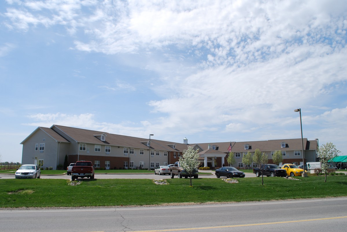 A large building with a parking lot in front, surrounded by grass and under a partly cloudy sky.