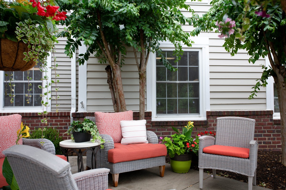 A cozy patio setup with cushioned chairs, a side table, and lush greenery.