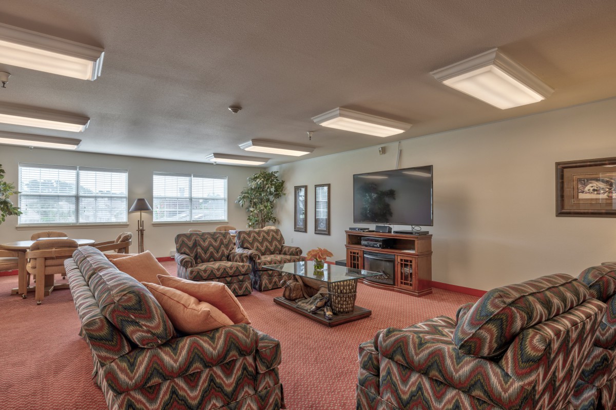 A cozy living room featuring patterned sofas, a large television, and a glass coffee table.