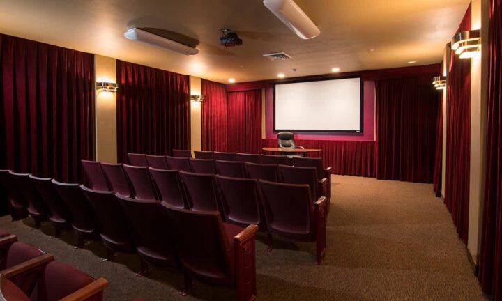 An empty theater room with rows of seats facing a large screen.