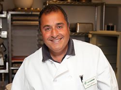 A smiling chef in a white uniform standing in a kitchen.