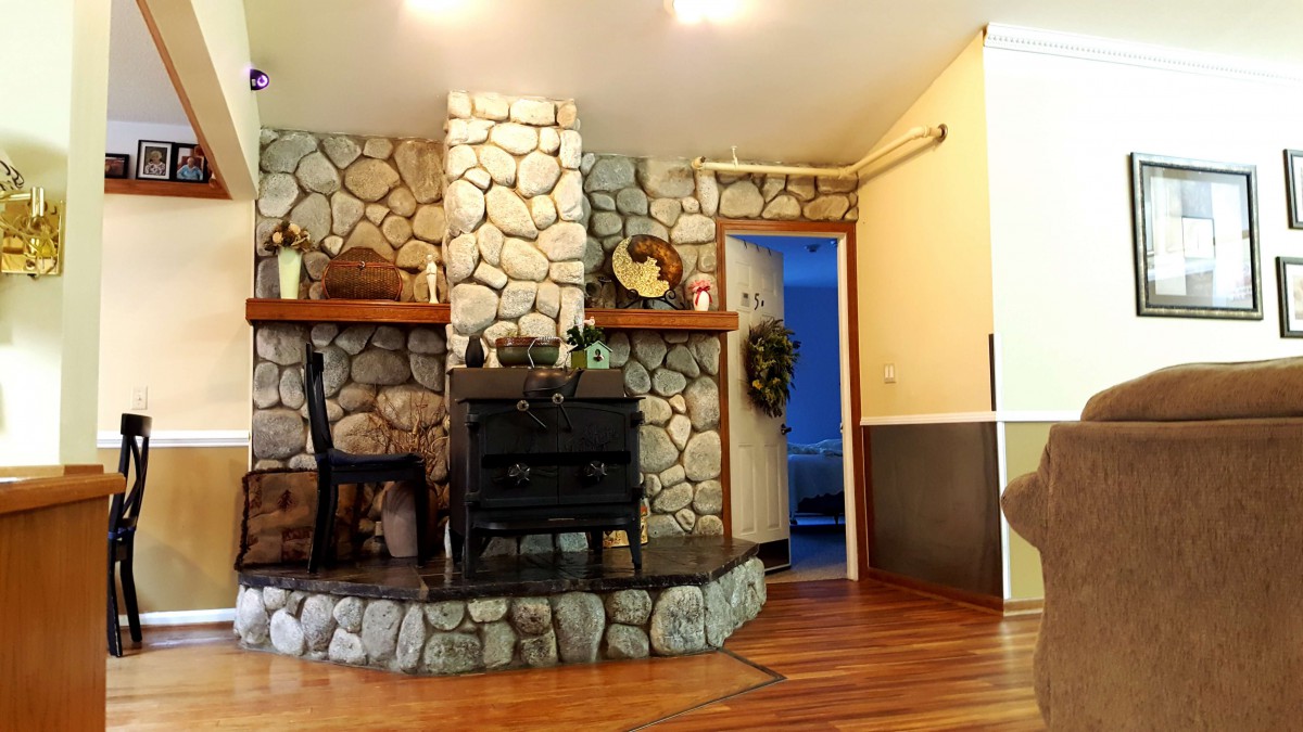A cozy living room with a stone fireplace and a wood stove, complemented by hardwood flooring.