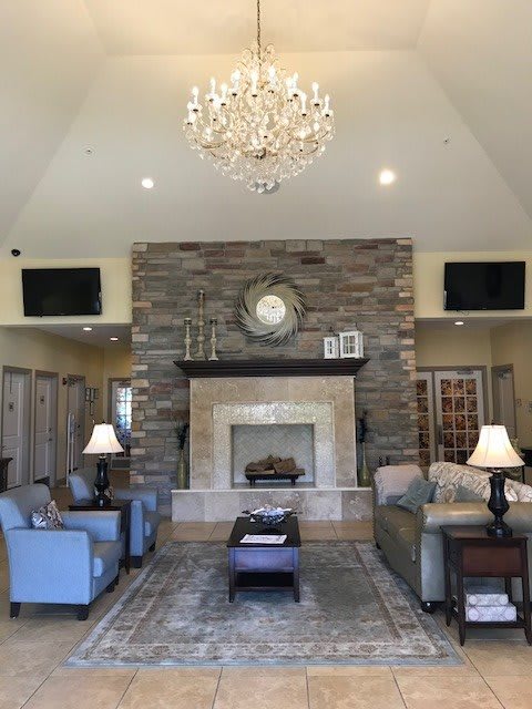 A cozy living room with a large stone fireplace, elegant chandelier, and plush seating.