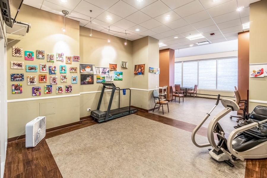 A well-lit indoor gym with a treadmill, exercise equipment, and seating area adorned with colorful artwork.