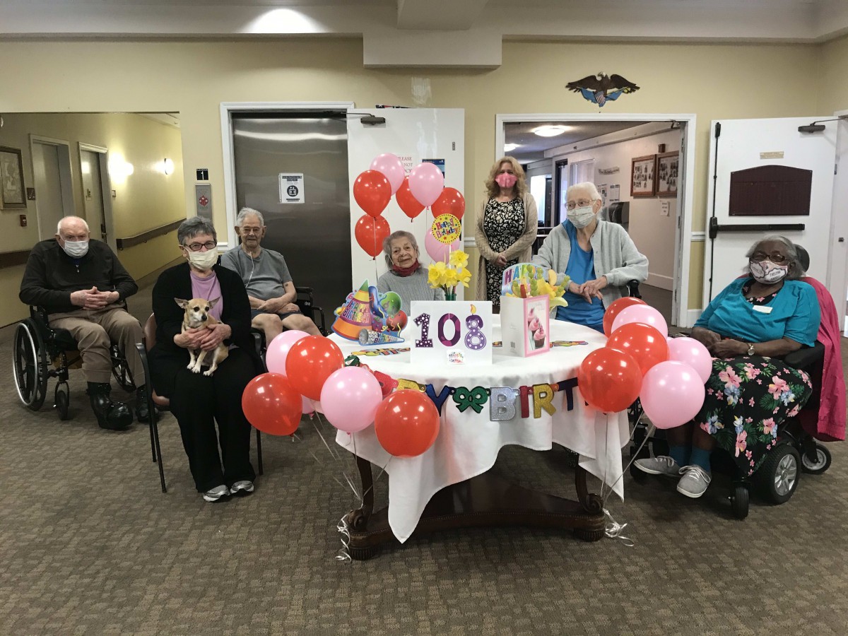 A group of elderly people celebrating a 108th birthday with balloons and a cake.