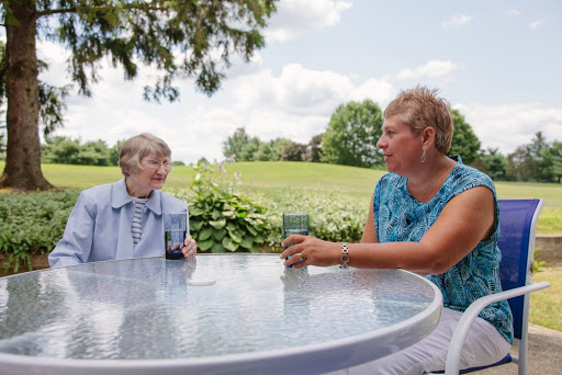Two women enjoying a summer afternoon conversation at a table outdoors, surrounded by lush greenery.