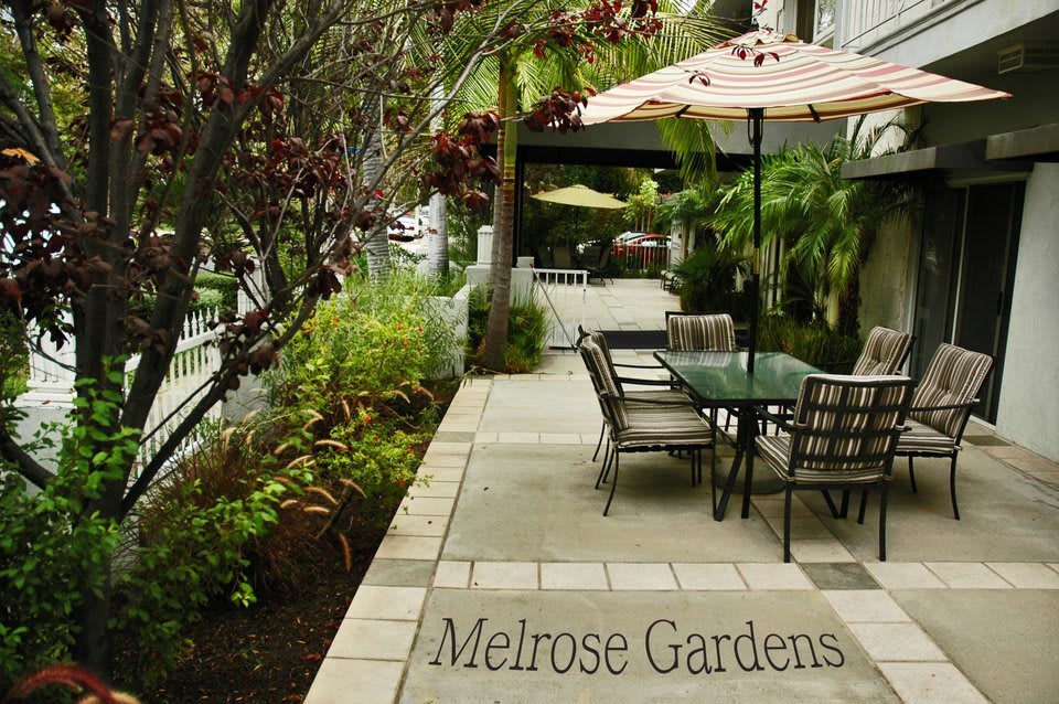A serene garden patio set with tables and umbrellas, surrounded by lush greenery.