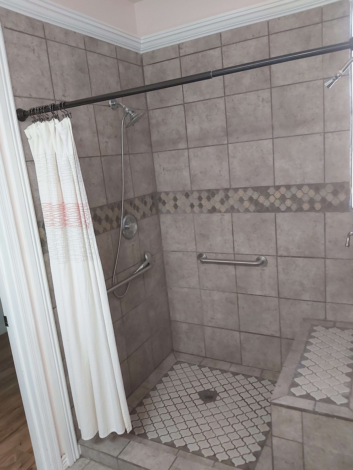 A tiled bathroom shower with a curtain and grab bars for accessibility.