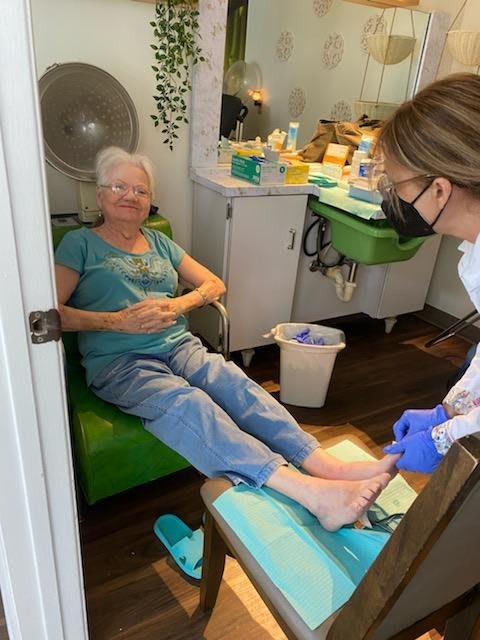 A senior woman receiving a pedicure from a healthcare professional in a salon.