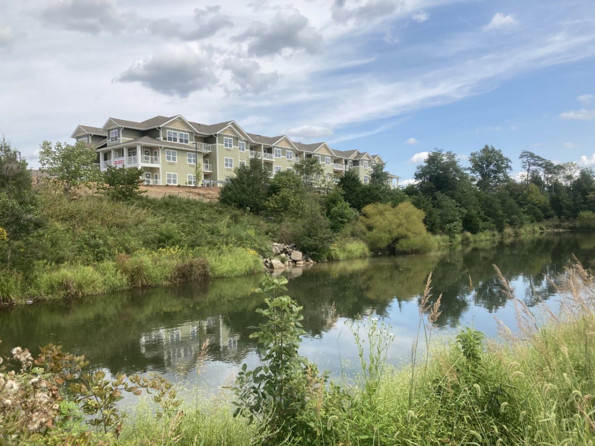 Scenic view of buildings overlooking a serene river with clear reflections and a cloudy sky.
