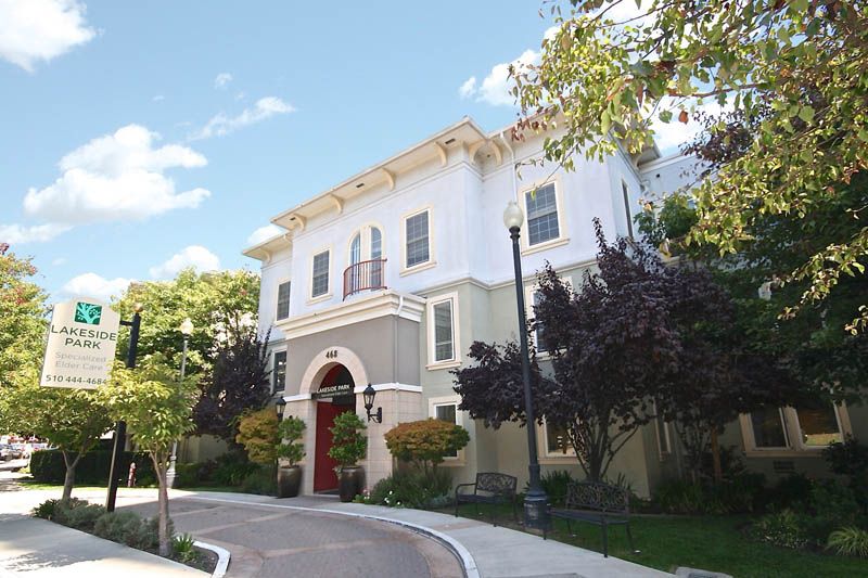 A three-story residential building surrounded by trees under a clear blue sky.