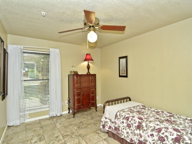 A cozy bedroom with a single bed, floral bedding, and a wooden chest of drawers under a warm lamp.