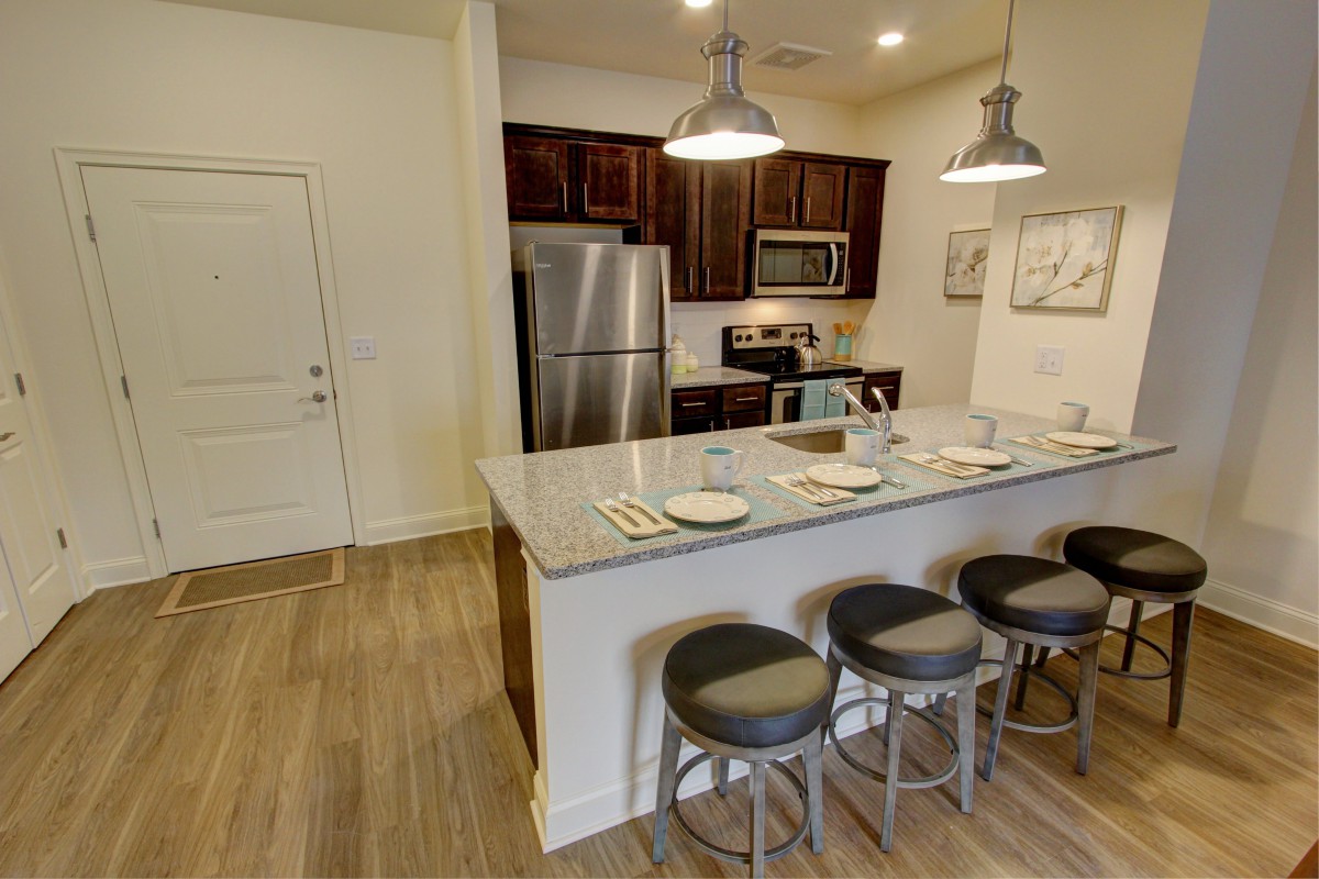 A modern kitchen with stainless steel appliances and a marble countertop with bar stools.
