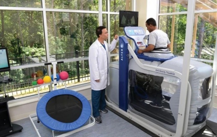 A healthcare professional assists a patient using a specialized treadmill for rehabilitation therapy.