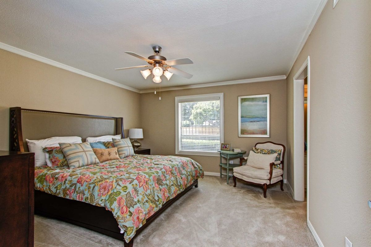 A cozy bedroom with a floral-patterned bedspread, framed artwork on the walls, and comfortable seating by the window.