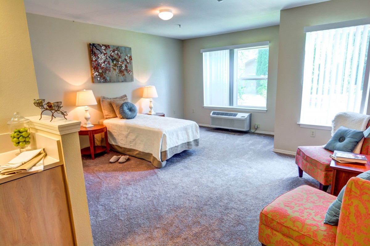 A cozy bedroom with a neatly made bed, soft lighting, and large windows.