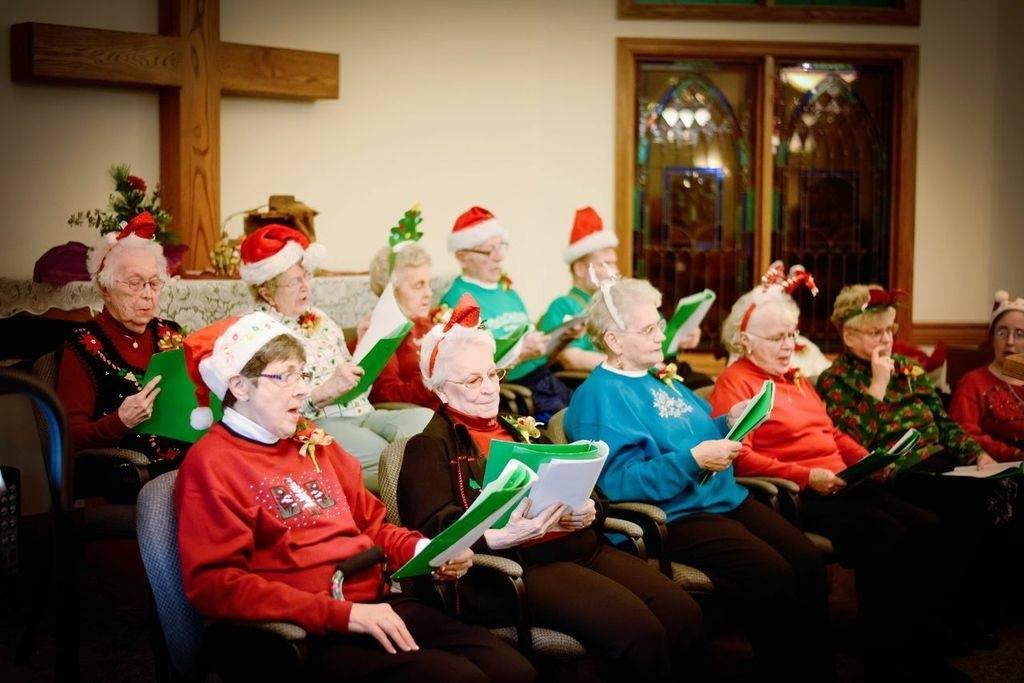 A group of elderly individuals singing in a choir, dressed in festive holiday attire.